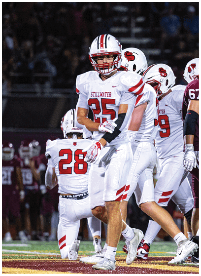 A person in a white football uniform with red accents is holding a football and appears to be running during a game. Description generated by AI