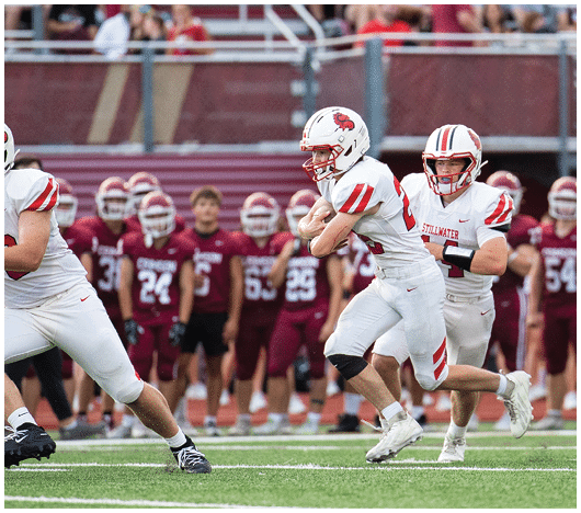 Two people wearing white football helmets with red faceguards and a red lion logo are focused and looking ahead. Description generated by AI