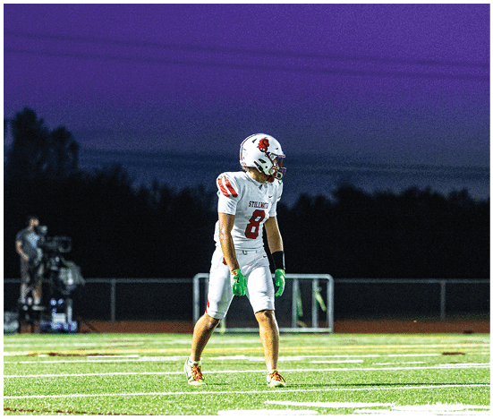 Two people wearing white football helmets with red faceguards and a red lion logo are focused and looking ahead. Description generated by AI
