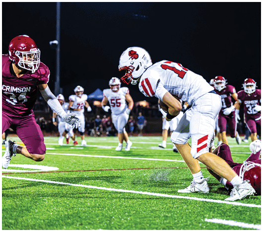 Two people wearing white football helmets with red faceguards and a red lion logo are focused and looking ahead. Description generated by AI