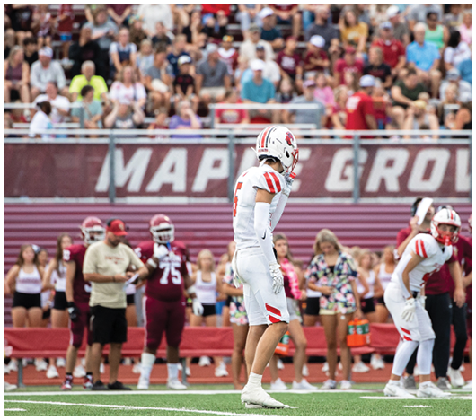 Two people wearing white football helmets with red faceguards and a red lion logo are focused and looking ahead. Description generated by AI