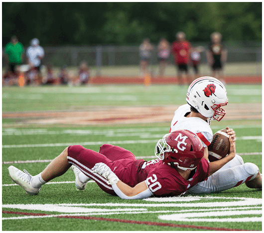 Two people wearing white football helmets with red faceguards and a red lion logo are focused and looking ahead. Description generated by AI