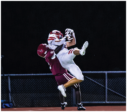 Several football players in helmets and uniforms are engaged in a tackle on a field with yard lines visible. Description generated by AI