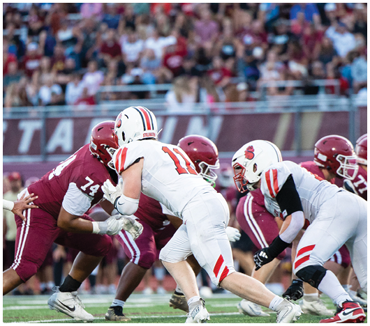 Several football players in helmets and uniforms are engaged in a tackle on a field with yard lines visible. Description generated by AI