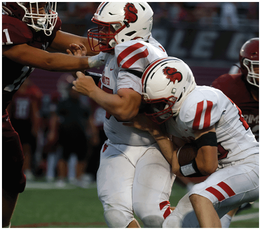 Two people wearing white sports uniforms with red stripes are engaged in a football play on a field. Description generated by AI