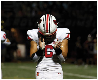 Two people in white sports uniforms stand on a football field, with one person clapping and the other facing away. Description generated by AI
