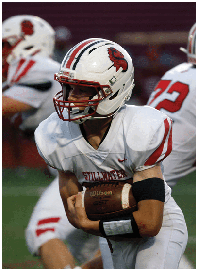 A person in a white football uniform with red accents is holding a football and appears to be running during a game. Description generated by AI