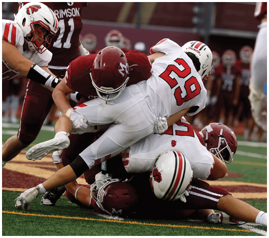 Several football players in helmets and uniforms are engaged in a tackle on a field with yard lines visible. Description generated by AI