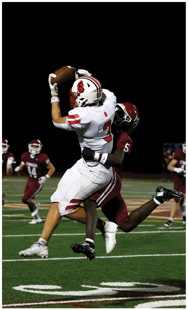 People in football uniforms are running on a field during a nighttime game. Description generated by AI
