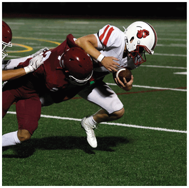 Two people in maroon football uniforms tackle a person in a white football uniform who is holding a football and running on a field. Description generated by AI