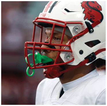 A person wearing a white football helmet with a red faceguard and a green mouthguard is looking intently to the side. Description generated by AI