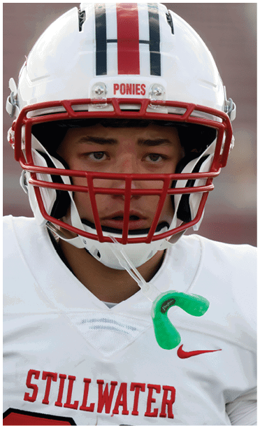 A person wearing a white football jersey with red lettering and a white helmet with a red faceguard is focused and has a green mouthguard hanging from the helmet. Description generated by AI