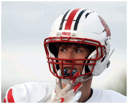 A person wearing a white football helmet with red faceguard and a white jersey is adjusting their chin strap while looking to the side. Description generated by AI
