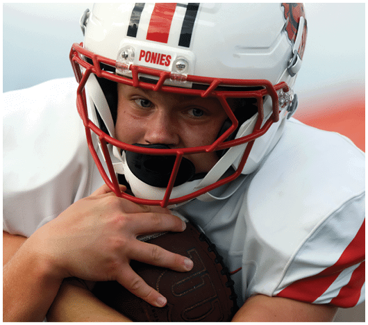 A person wearing a white football helmet and uniform tightly holds a football while looking ahead with focus. Description generated by AI