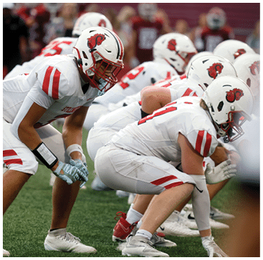 People in white and red football uniforms are crouched in a ready position on a grassy field. Description generated by AI