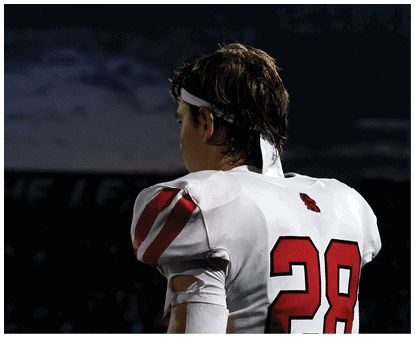 A person wearing a white and red football uniform with the number 2 on the back is standing and looking to the side against a dark, cloudy sky. Description generated by AI