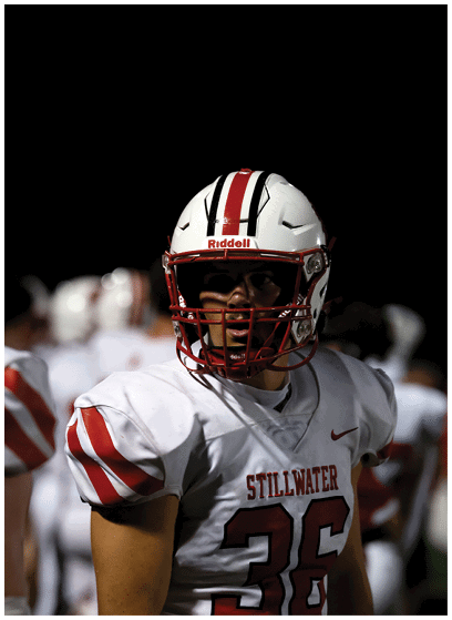 A person wearing a white football uniform with red stripes and the number 36 stands on a field at night with other players blurred in the background. Description generated by AI