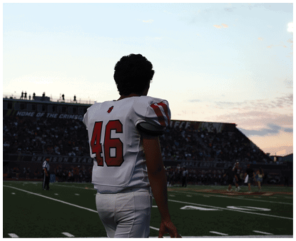 A person wearing a white sports jersey with the number 46 is standing and looking towards a stadium filled with spectators during sunset. Description generated by AI