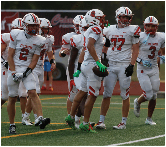 A group of people wearing white football uniforms with red accents and helmets are standing and walking on a football field. Description generated by AI