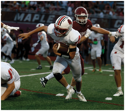 A person in a white football uniform is running with the ball while being pursued by a person in a maroon uniform on a football field. Description generated by AI