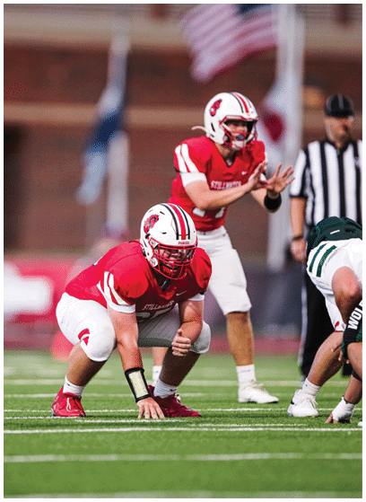 A person wearing a green and white football uniform with the number 19 and the word “WOLFPACK" on the pants is standing on a football field. Description generated by AI