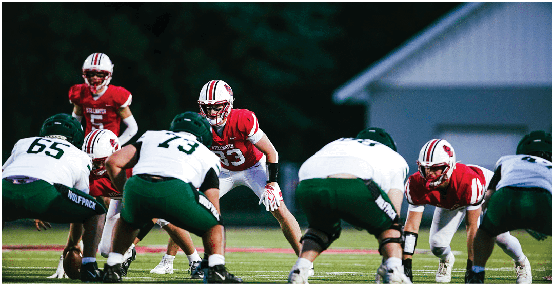 Adults in football uniforms are positioned on a field facing each other, preparing for a play during a nighttime game. Description generated by AI