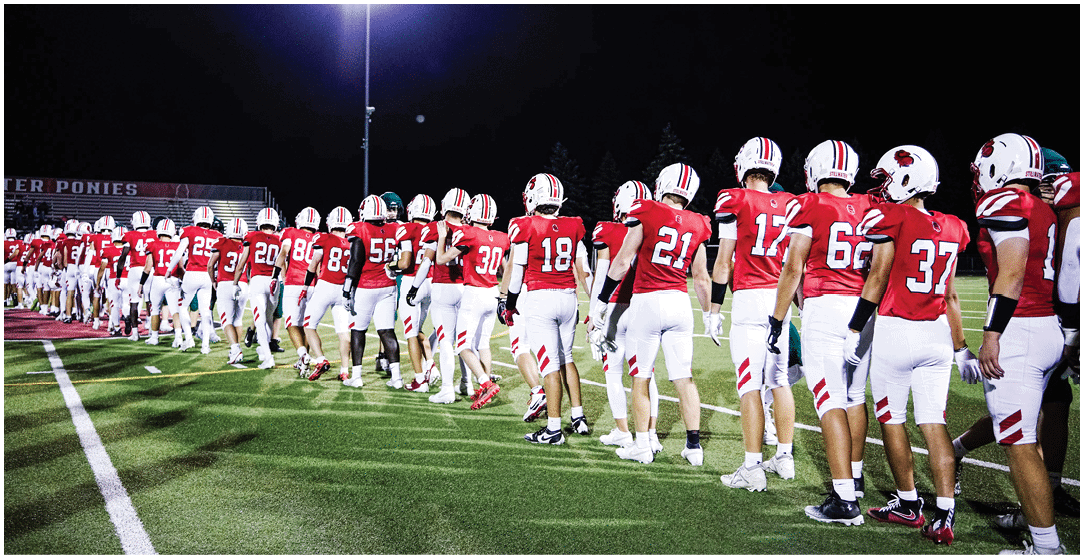 A line of people wearing red and white football uniforms are standing on a field at night, facing away from the camera. Description generated by AI