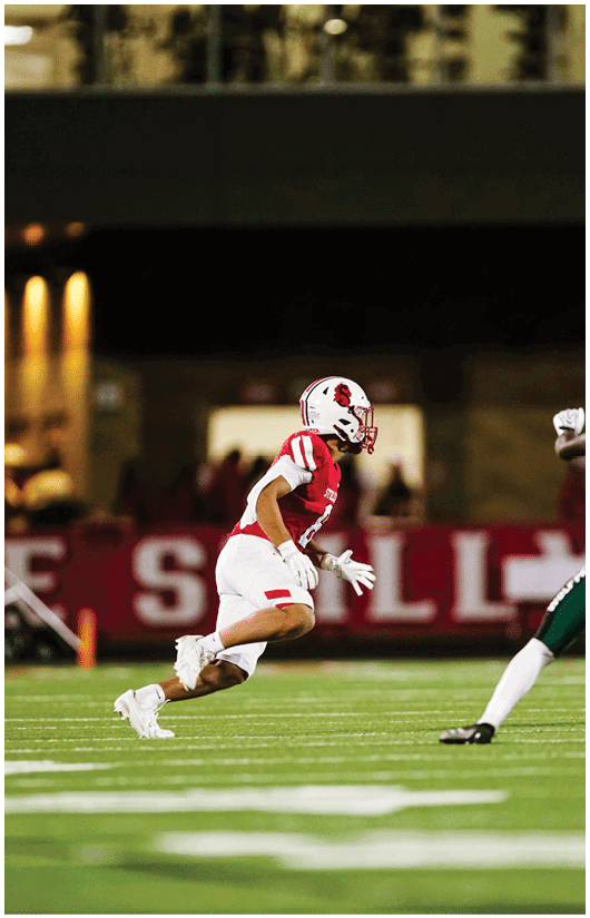 Two people in football uniforms are on a field with one running toward the other who is preparing to block or tackle. Description generated by AI