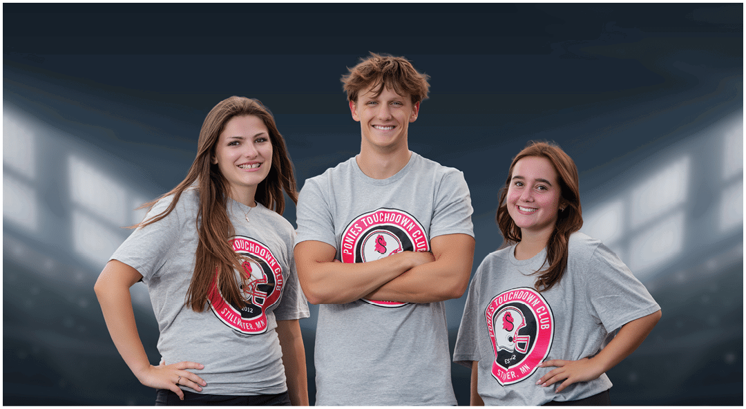Three smiling adults wearing matching gray t-shirts with a sports logo and black shorts or skirts stand confidently on a football field under stadium lights. Description generated by AI
