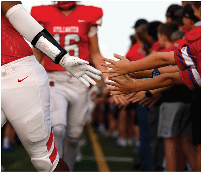 A person in a red football jersey and white pants is reaching out to high-five a line of people extending their hands. Description generated by AI