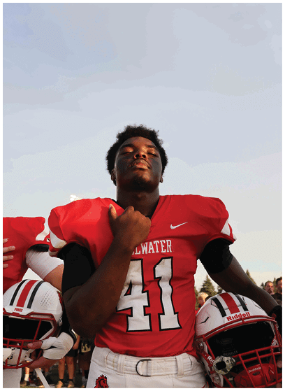 Two people wearing red football uniforms stand with their hands over their chests against a clear sky. Description generated by AI
