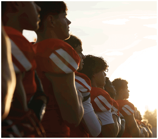 A line of people wearing red and white football uniforms stand side by side facing the sunlight. Description generated by AI