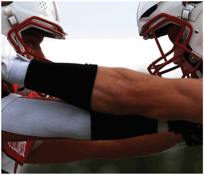 A group of people wearing white football uniforms with red and black accents are gathered closely together on a green field, appearing to be in a team huddle. Description generated by AI