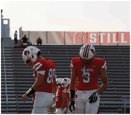 A person wearing a red football jersey with the number 10 and the word Stillwater is captured in an action pose. Description generated by AI
