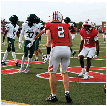 Two teams of people in football uniforms are on a field with one team in red and white and the other in green and white, appearing to prepare for a play. Description generated by AI