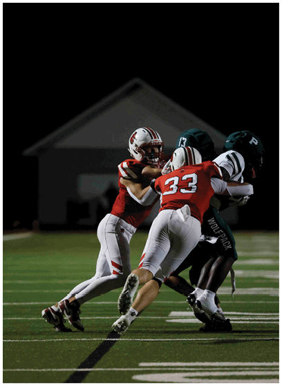 Two people in football uniforms are engaged in a play on a well-lit field at night with a building in the background. Description generated by AI