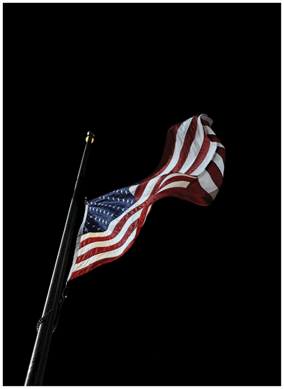 An American flag is flying at half-mast against a dark night sky. Description generated by AI
