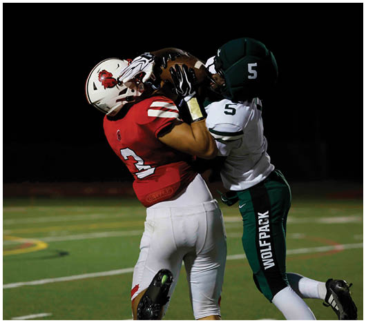 Two people in football uniforms are engaged in a tackle on a grassy field at night. Description generated by AI