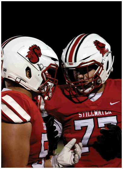People wearing red football uniforms and white helmets with a red logo are engaged in a discussion on the field at night. Description generated by AI