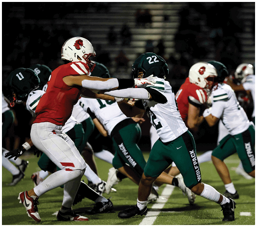 Several people in football uniforms are engaged in a play on a field under stadium lights. Description generated by AI