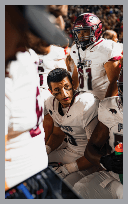 A group of people in football uniforms are gathered closely, with one person sitting and looking attentively while others stand around. Description generated by AI
