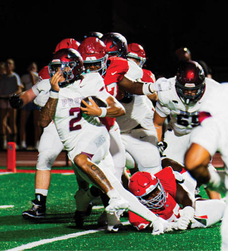 A group of people wearing football uniforms are actively engaged in a play on a green field under stadium lights. Description generated by AI