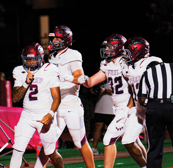 Three football players in white uniforms and helmets are celebrating near a goalpost on a field at night. Description generated by AI