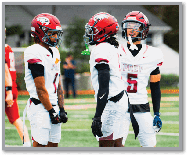 Three people wearing red helmets and white football jerseys with the word “PREP" are standing outdoors, seemingly engaged in conversation or preparing for a game. Description generated by AI
