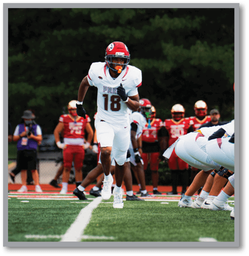 A person in a white football uniform with the number 18 is running on a field while other players and people stand in the background. Description generated by AI
