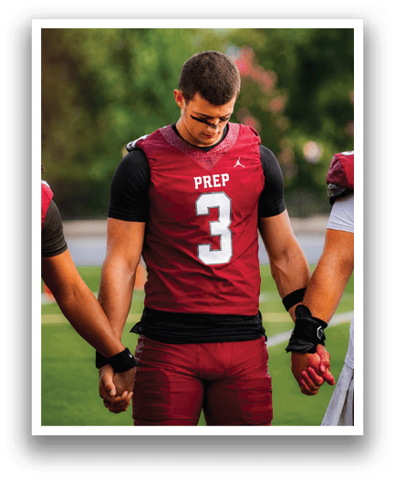 Two people wearing maroon football uniforms hold hands while standing on a field, with one looking down. Description generated by AI