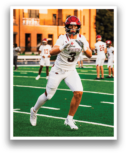 A person in a white football uniform with the number 3 is running on a green field with other players and a building in the background. Description generated by AI