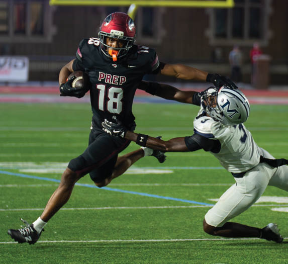 A person wearing a black football uniform with the word “PREP" and number 18 is running with a football while extending an arm to fend off another player in a white helmet. Description generated by AI
