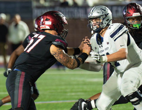 Two people in football uniforms are engaged in a blocking stance on a football field during a game. Description generated by AI