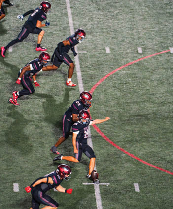 Several people in football uniforms are running on a field as one person kicks a football. Description generated by AI